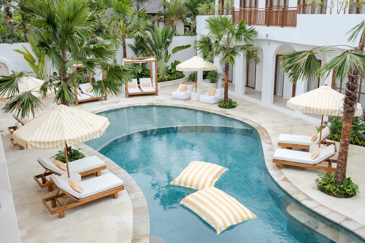 Peaceful swimming pool with lounge pillows surrounded by lush tropical trees at a Bali yoga and spa retreat.