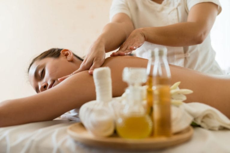 Therapist massaging a woman’s back, with herbal compress balls and massage oils in the foreground