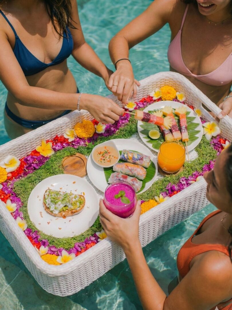 Women enjoying a colorful floating breakfast with tropical fruit and fresh juices in a Bali pool.
