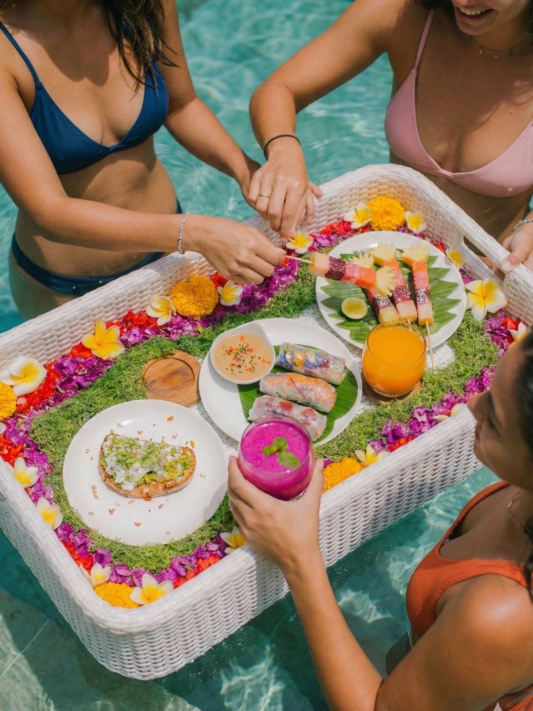 Women enjoying a colorful floating breakfast with tropical fruit and fresh juices in a Bali pool.