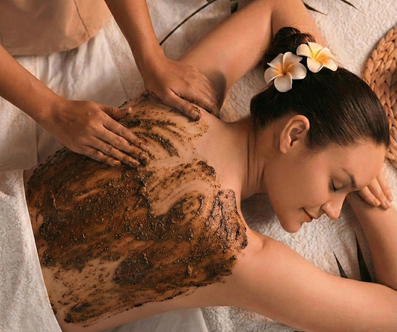 A professional Indonesian spa practitioner applying a traditional warming Boreh spice scrub to the back of a woman for skin rejuvenation and muscle relief during a luxury Bali wellness retreat.