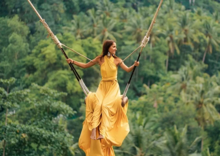 Woman in a yellow dress sitting on a swing surrounded by lush tropical trees at a holistic wellness retreat.
