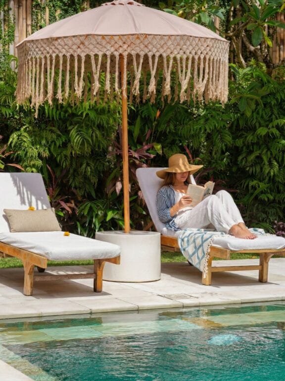 Woman reading and relaxing on a lounge chair by the pool at a Bali wellness retreat.