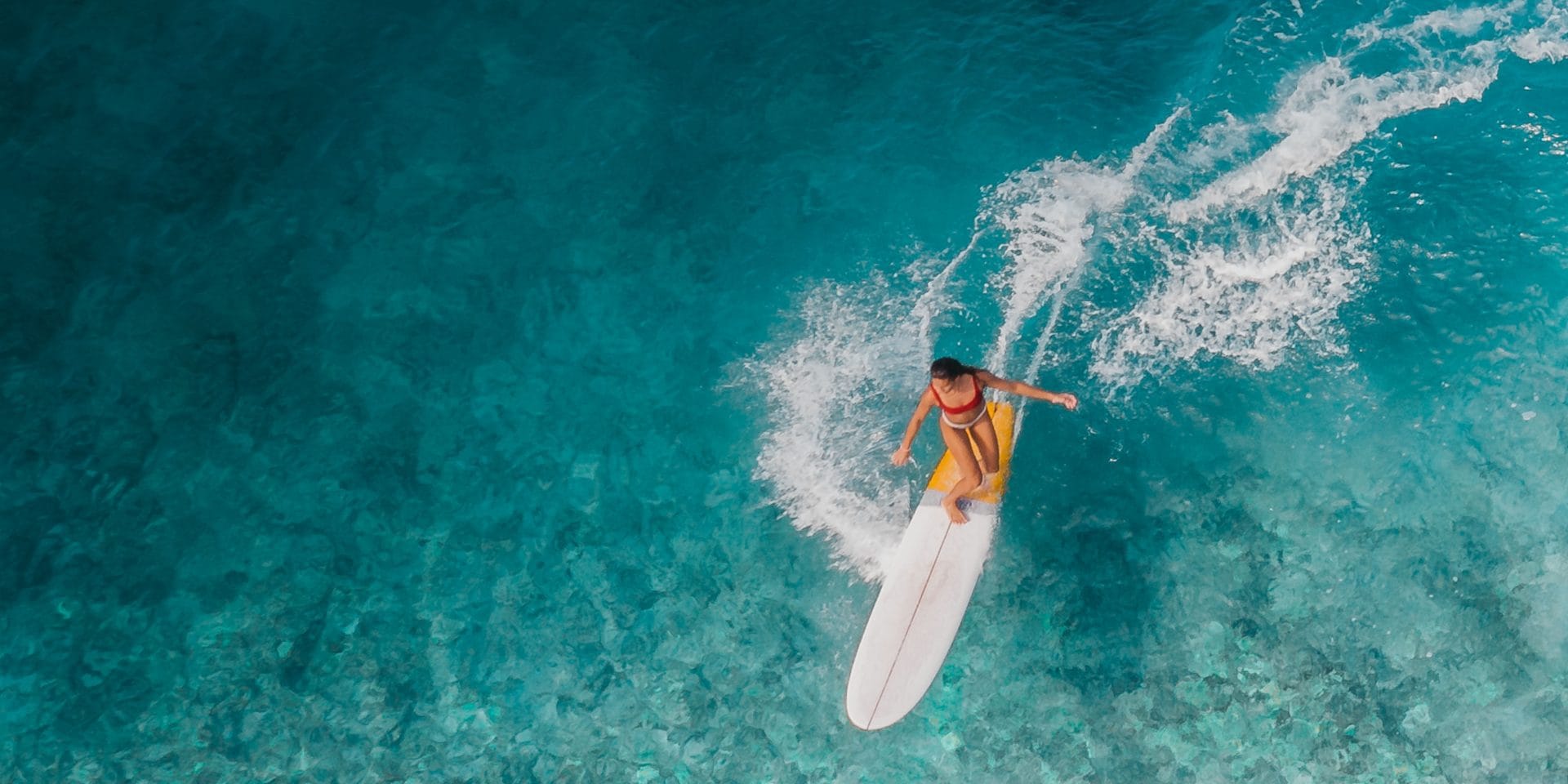 Smiling woman surfing on a vibrant wave, embodying the spirit of a Surf Goddess at Goddess Retreats, with the ocean and sky in the background.