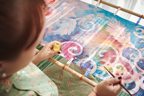 Girl painting ornament on textile, view over the shoulder