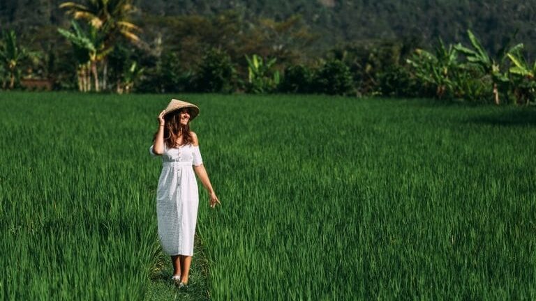 woamn walking through rice paddies on a sunny day in bali while on a cultural bali wellness retreat