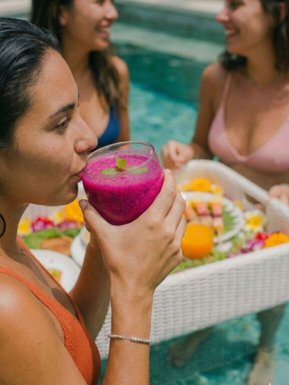 Woman enjoying a dragon fruit smoothie beside the pool at a Bali women’s wellness retreat.