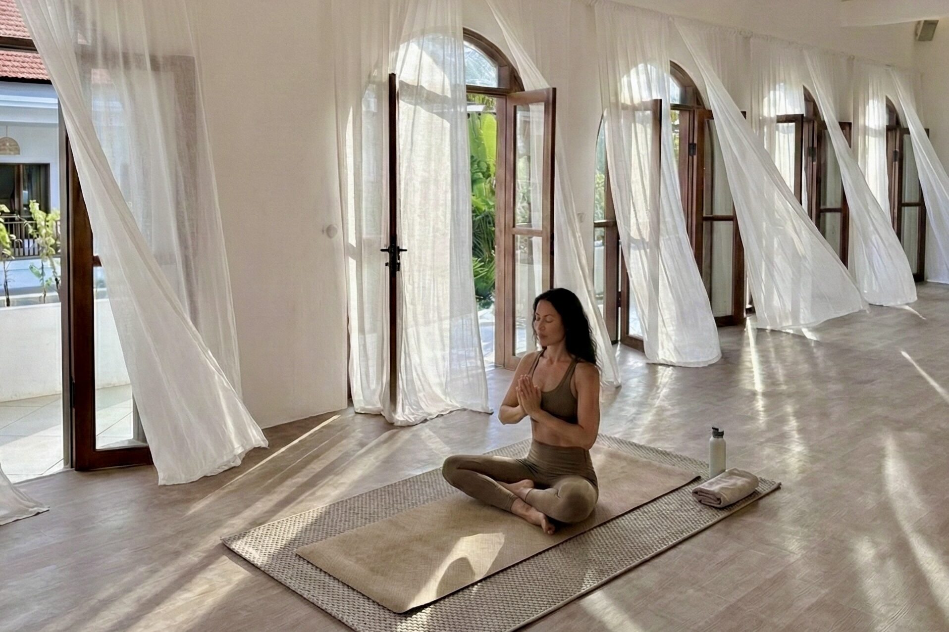 A woman sitting in quiet meditation with prayer hands in the serene, open-air yoga shala at Goddess Retreat, Bali.